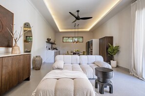 Ein modernes Wohnzimmer mit einem Ecksofa, einem Deckenventilator, Pendelleuchten und einem großen Fenster.