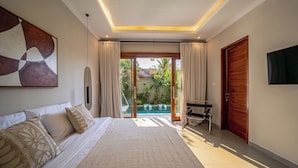 Un dormitorio con cama, televisión, escritorio y vistas a una piscina al aire libre.