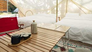 Un hébergement sous tente comprenant un lit, une table avec des tasses et une chaise rouge.