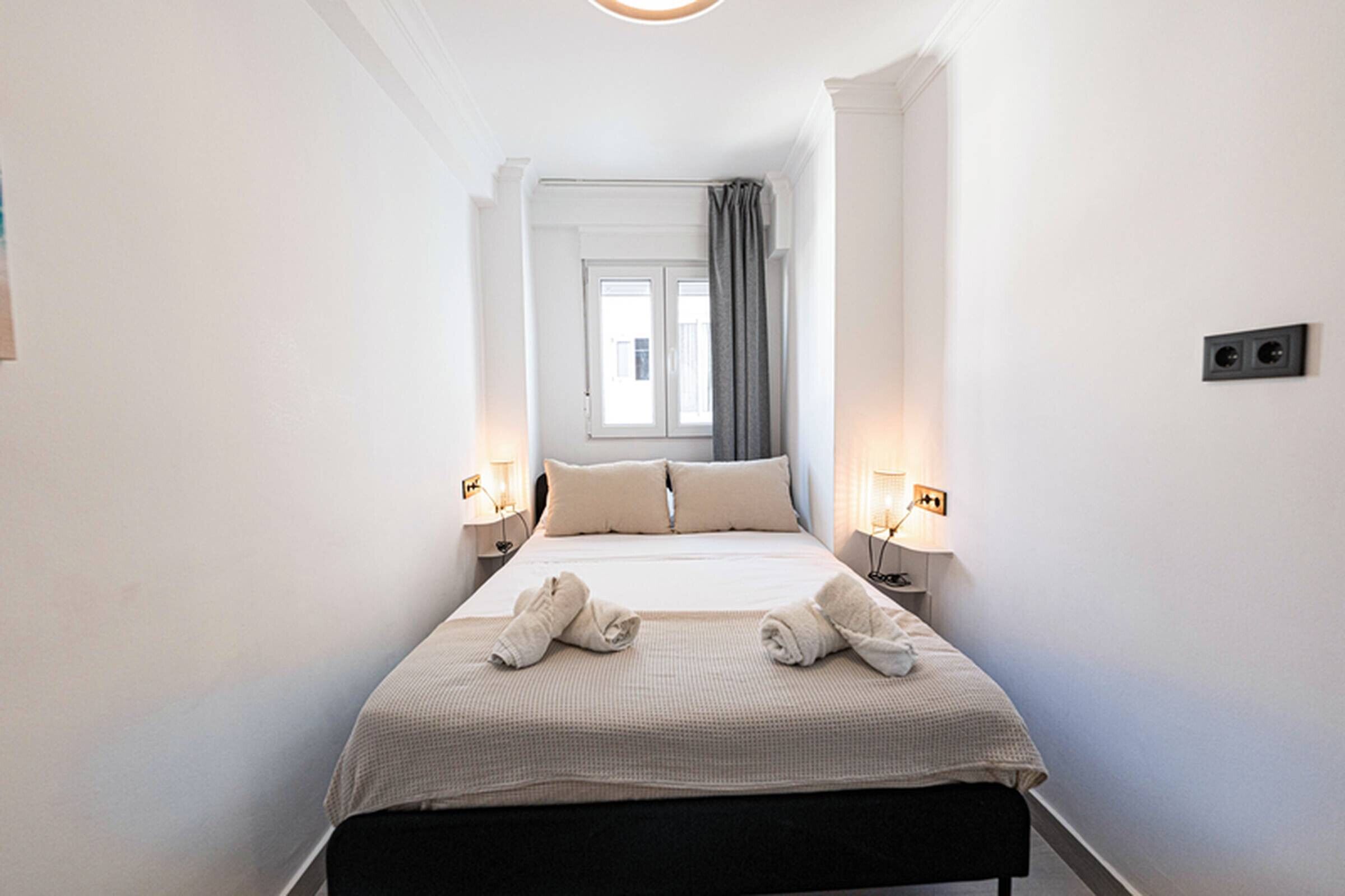 Une chambre d’hôtel avec un lit, deux lampes de chevet, une fenêtre avec des rideaux et un interrupteur fixé au mur.