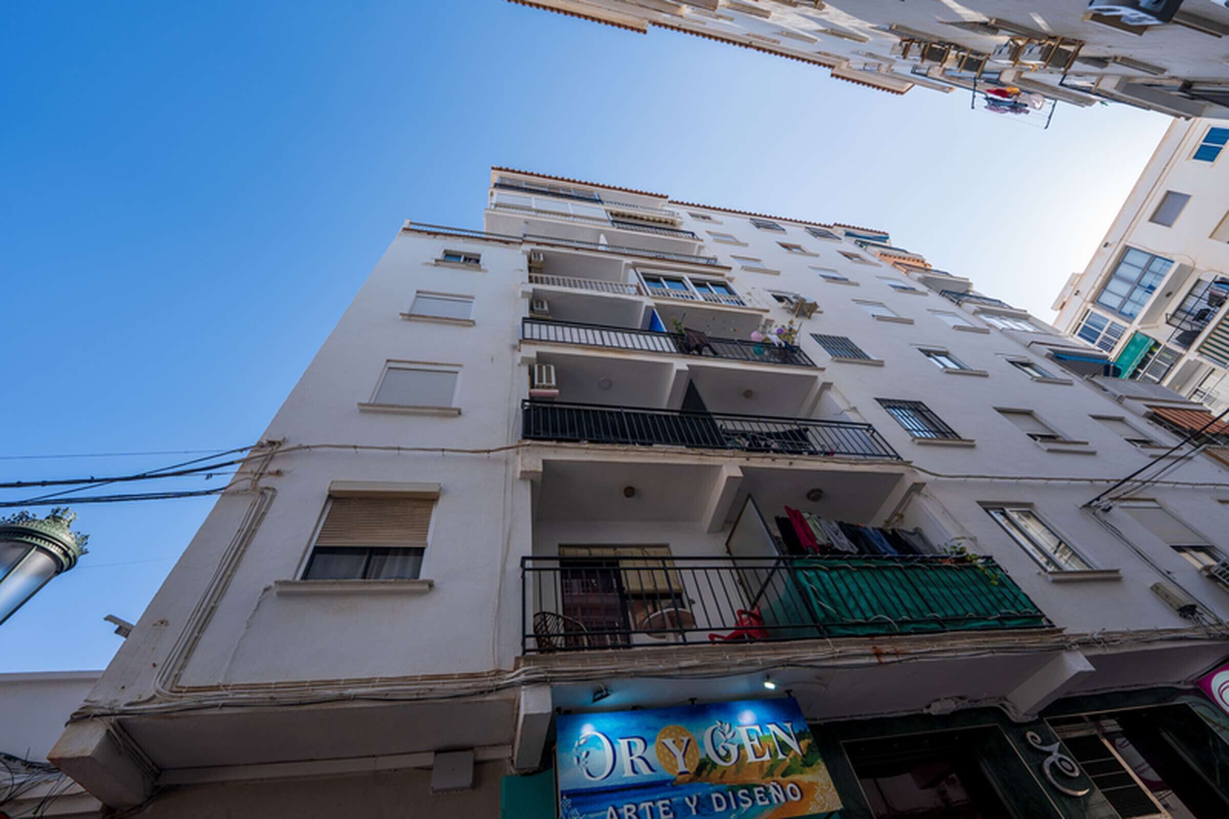Un immeuble à plusieurs étages doté de balcons, avec une enseigne de magasin bien visible, et un ciel dégagé.