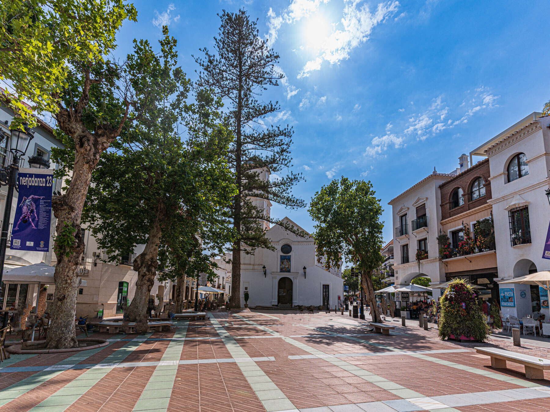 A plaza with a tiled floor, trees, and buildings with balconies.