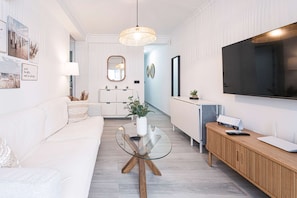 Ein modernes Wohnzimmer mit Glastisch, weißem Sofa, Holzschrank und einem an der Wand befestigten Fernseher.