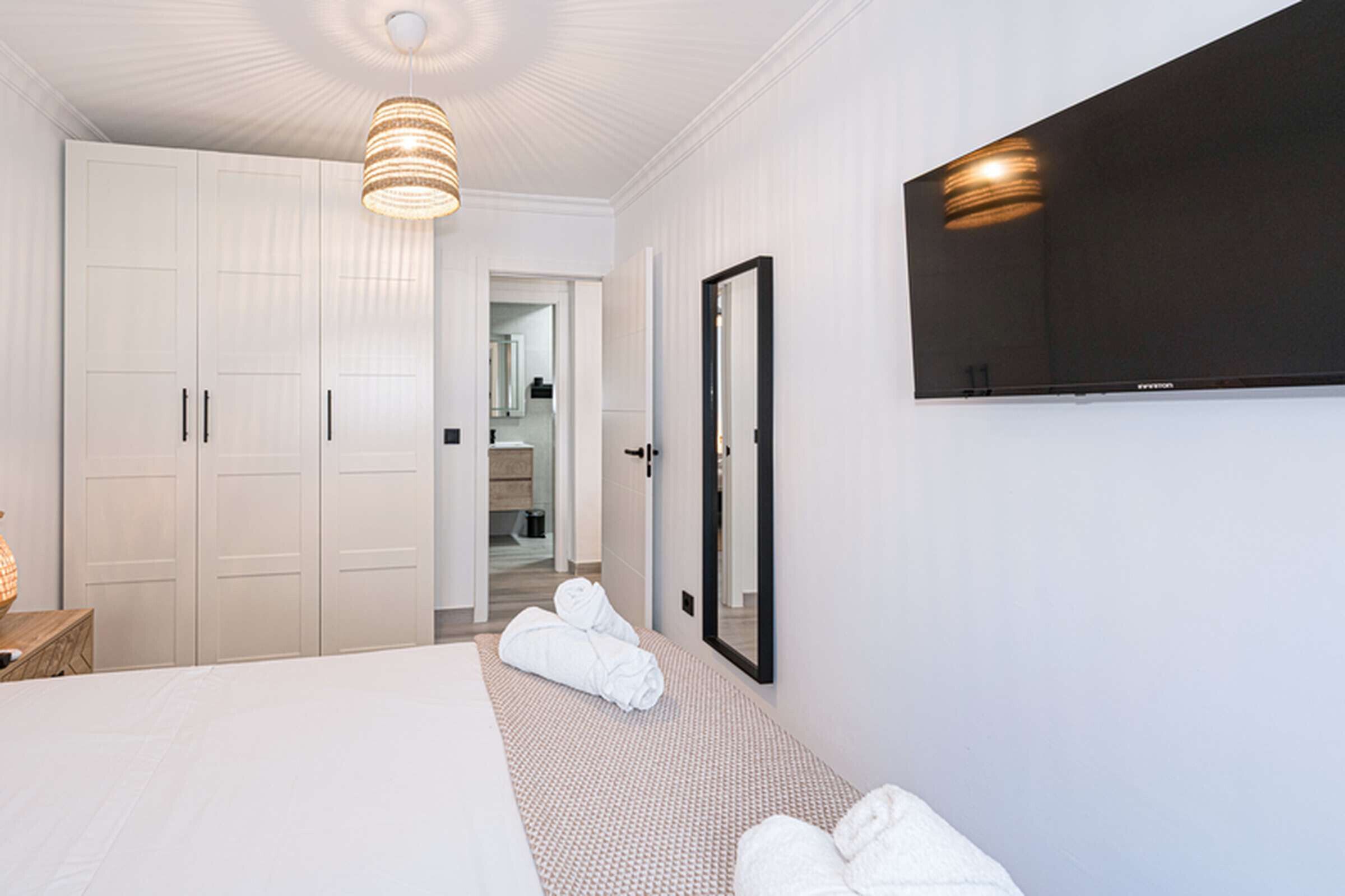 A hotel room with a large bed, a television mounted on the wall, a wardrobe, and a mirror.