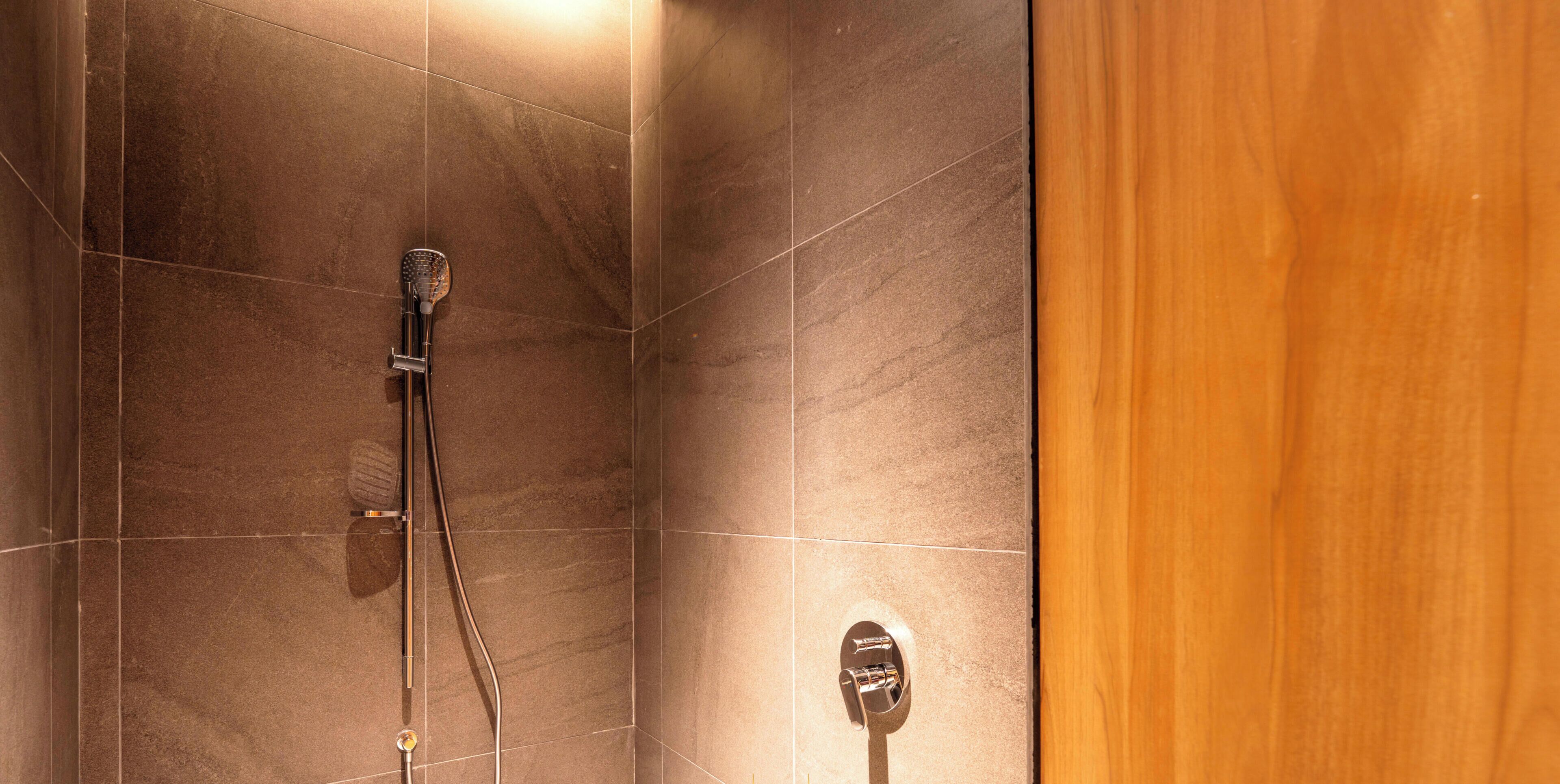 A shower with a handheld showerhead and a wall-mounted control panel.