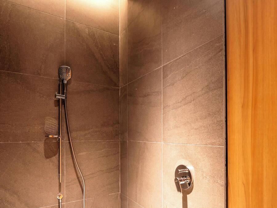 A shower with a handheld showerhead and a wall-mounted control panel.