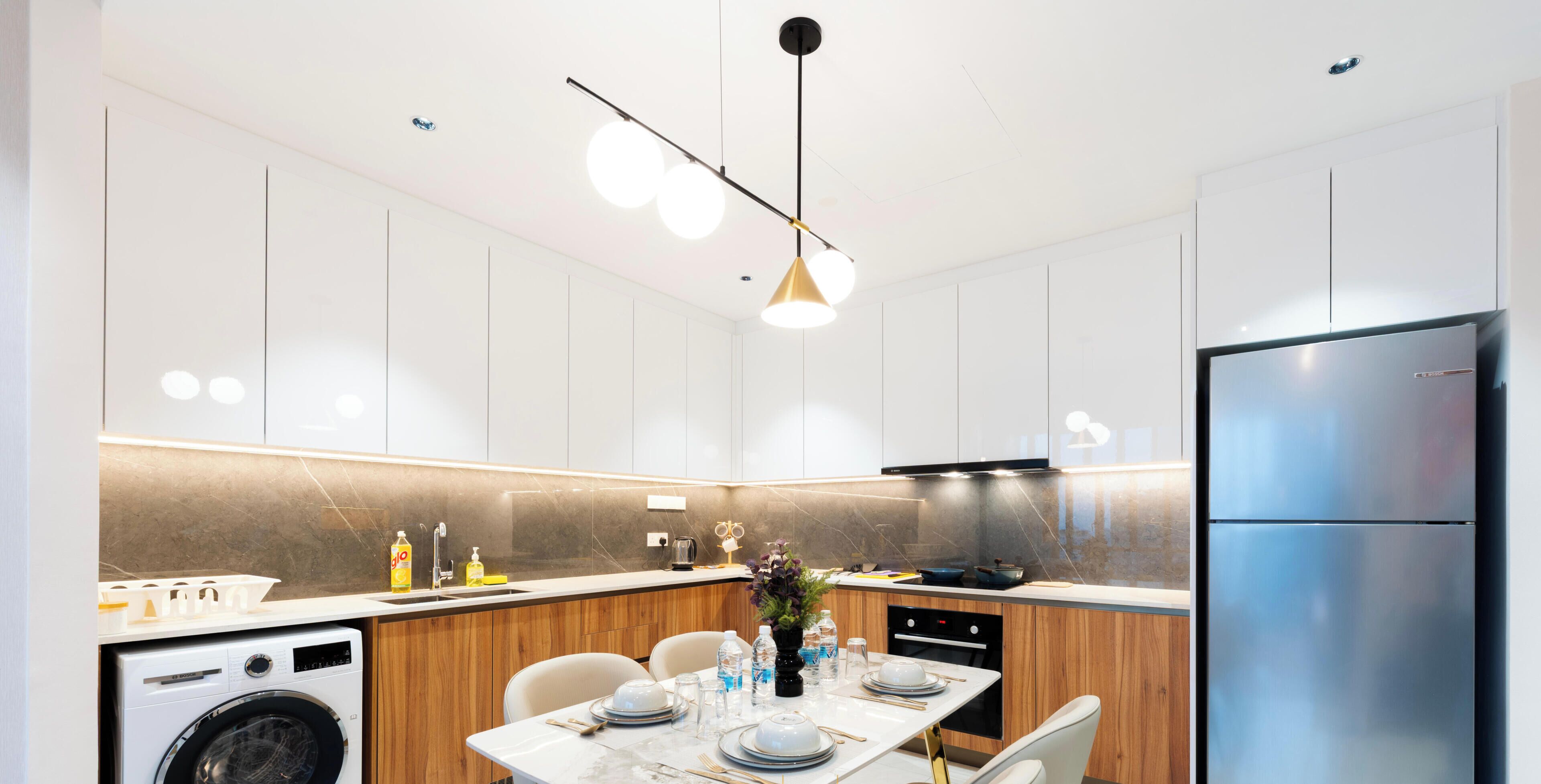 A modern kitchen with a built-in washing machine, wooden cabinetry, a stainless steel refrigerator, and a dining area with a marble table.