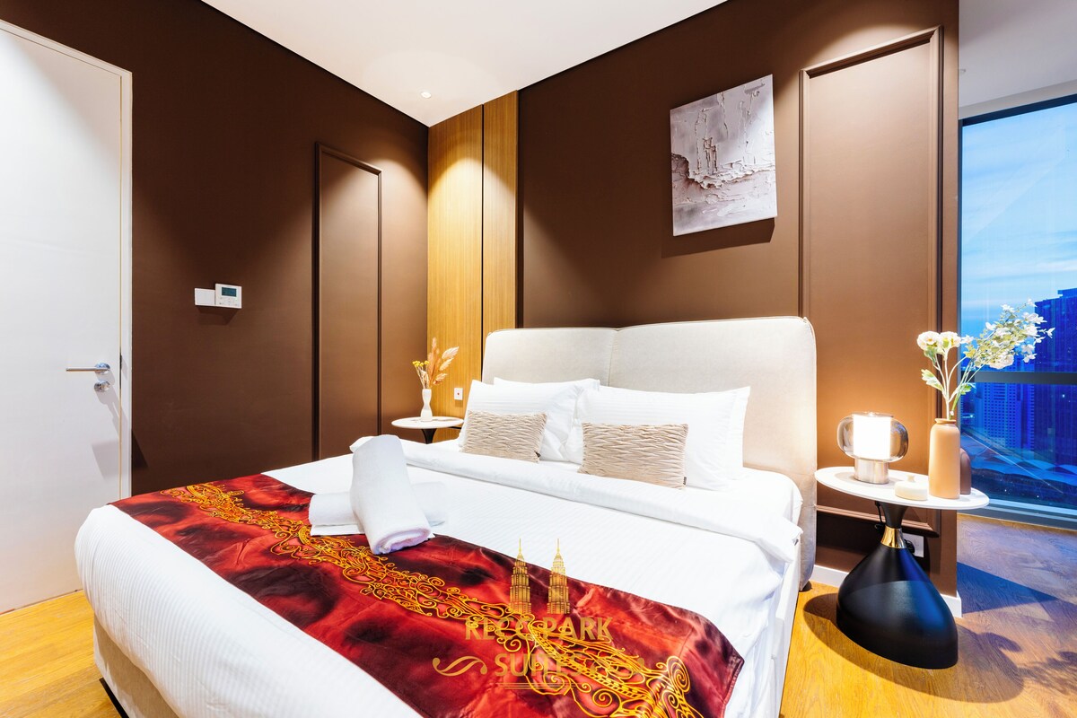 Una habitación de hotel con una cama grande, una mesita de noche con lámpara, un jarrón con flores y vistas a la ciudad.