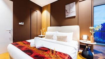 A hotel room with a large bed, a nightstand with a lamp, a vase with flowers, and a view of the city.