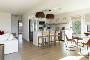 A modern kitchen with a central island, wooden chairs, and a dining table with chairs. - The SouthOhana Beach House with Ocean Views! (Oceanside)
