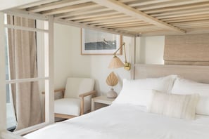 A bedroom with a bed, a chair, a nightstand, a lamp, and a framed picture on the wall. - The SouthOhana Beach House with Ocean Views! (Oceanside)