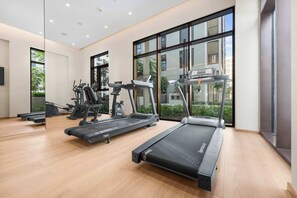 Ein modernes Fitnessstudio mit Laufbändern, Crosstrainern und Kraftgeräten, großen Fenstern und Holzboden.