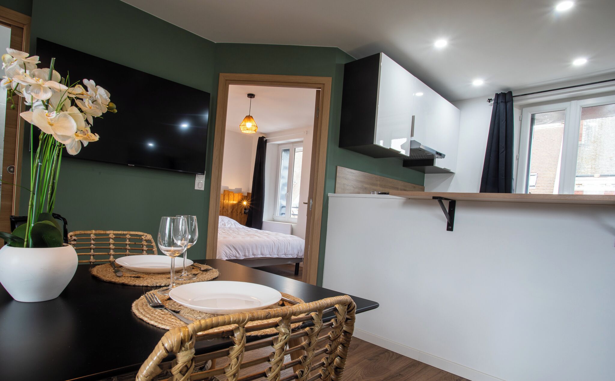 Een eetgedeelte met een donker houten tafel, twee rieten stoelen, een vaas met witte bloemen en een wijnglas.