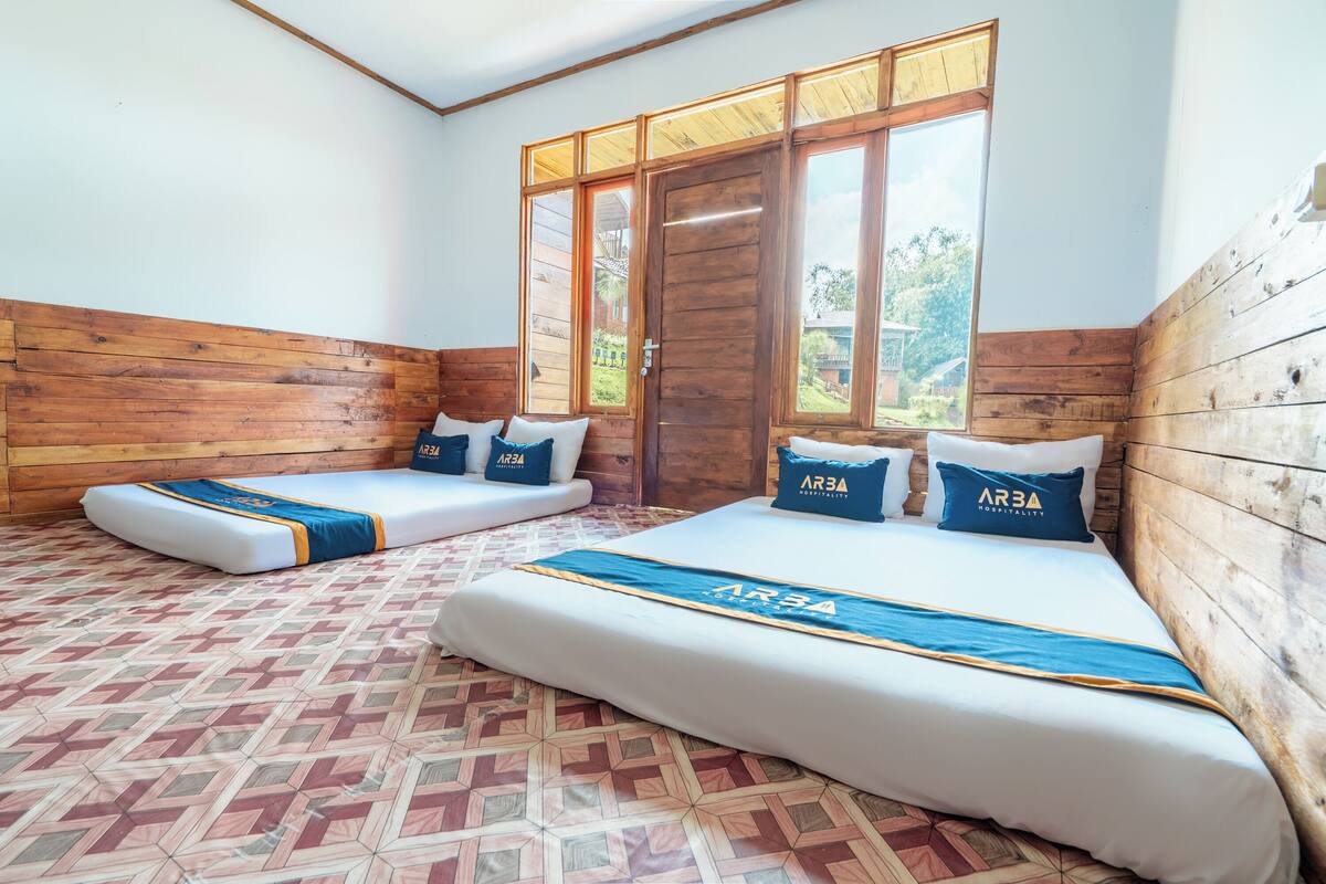 Una habitación con dos camas, paredes de madera, ventanas amplias y suelo estampado.
