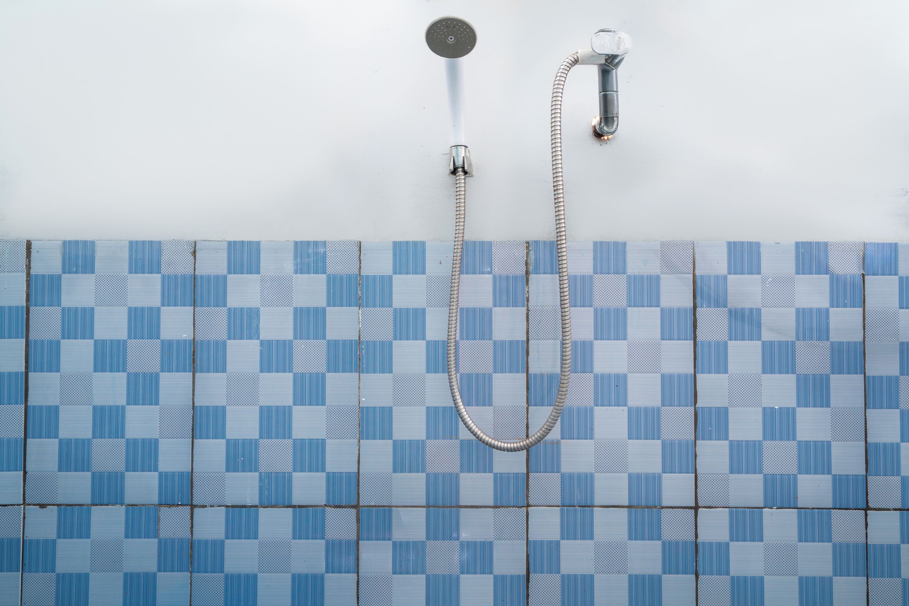 Een badkamer met een douche, betegelde wand en een zichtbare douchekop.