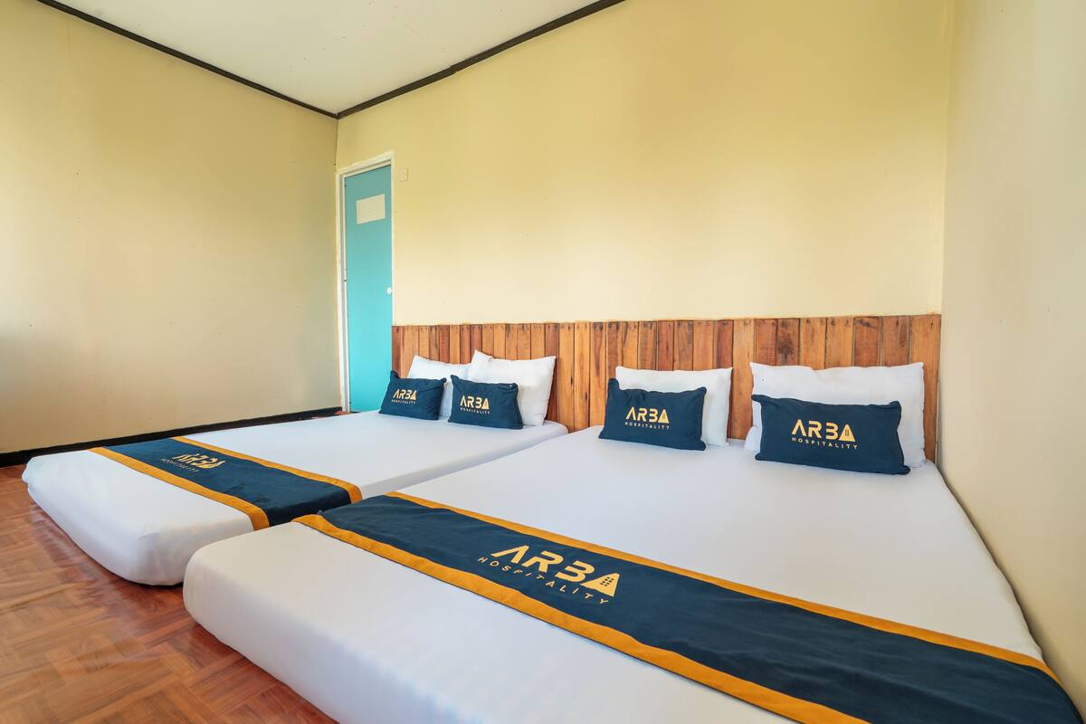 Habitación de hotel con dos camas, cada una con colcha y almohadas a juego, y cabeceros de madera.
