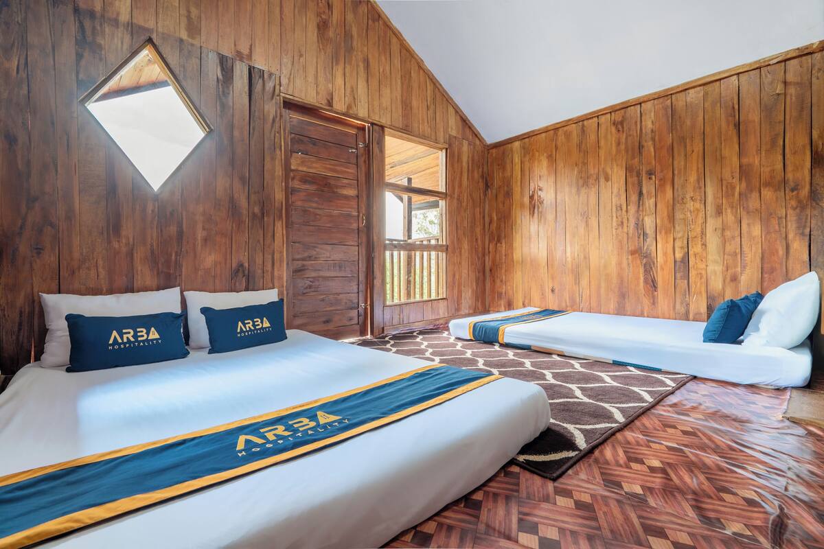 Habitación de hotel con paredes de madera, una cama con edredón de marca, un sofá y una ventana.