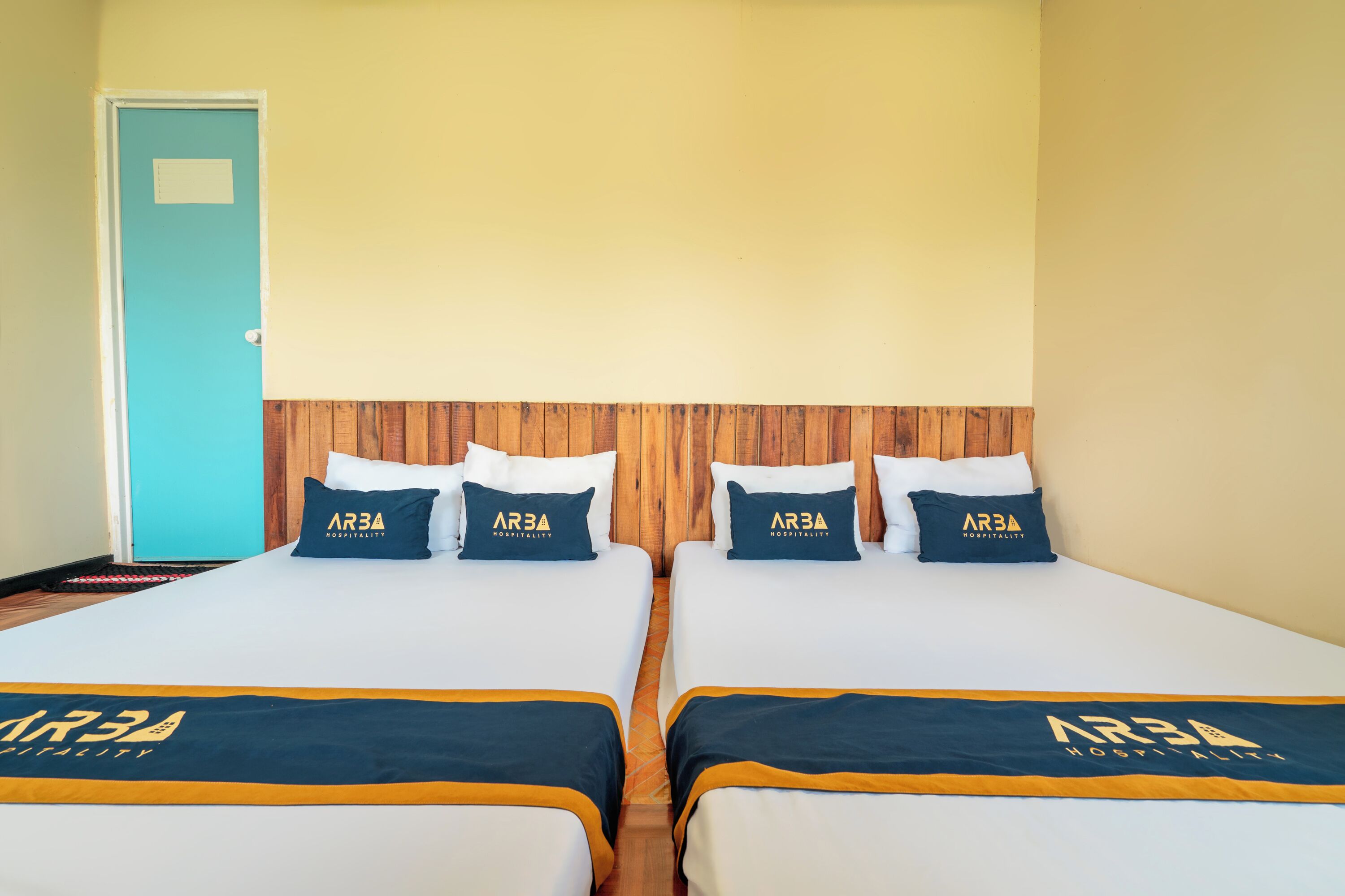 A hotel room with two beds, each with a matching pillow and bedspread featuring the hotel's logo.