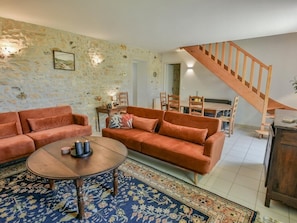 Ein Wohnzimmer mit Sofa, Couchtisch und einem gemusterten Teppich. Eine Treppe führt zu einem anderen Raum.