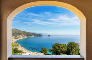 Vista costera a través de un ventanal arqueado, cielo despejado y mar en calma.