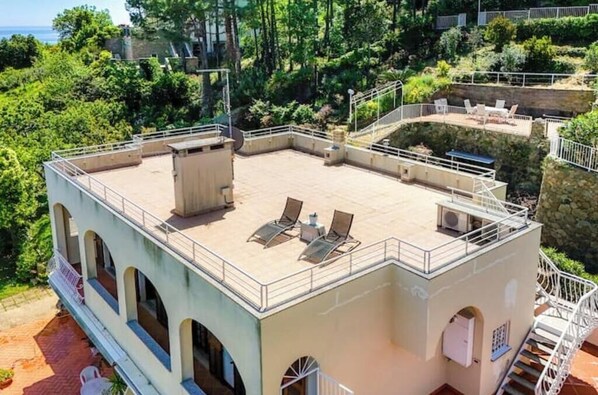 Una terraza en la azotea con sillones de sol, una pequeña mesa y una escalera que sube a un nivel superior.
