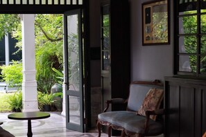 Une porte ouverte donnant sur un jardin luxuriant, une chaise en bois avec un coussin et un tableau encadré accroché au mur.