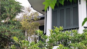 Ein Gebäude mit weißer Fassade und dunklen Fensterläden, umgeben von üppiger Vegetation.