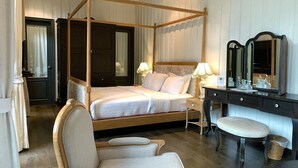 Ein Bett mit Baldachin und Holzrahmen, ein Nachttisch mit Lampe, ein Stuhl, ein kleiner Hocker und eine Kommode mit Spiegel.