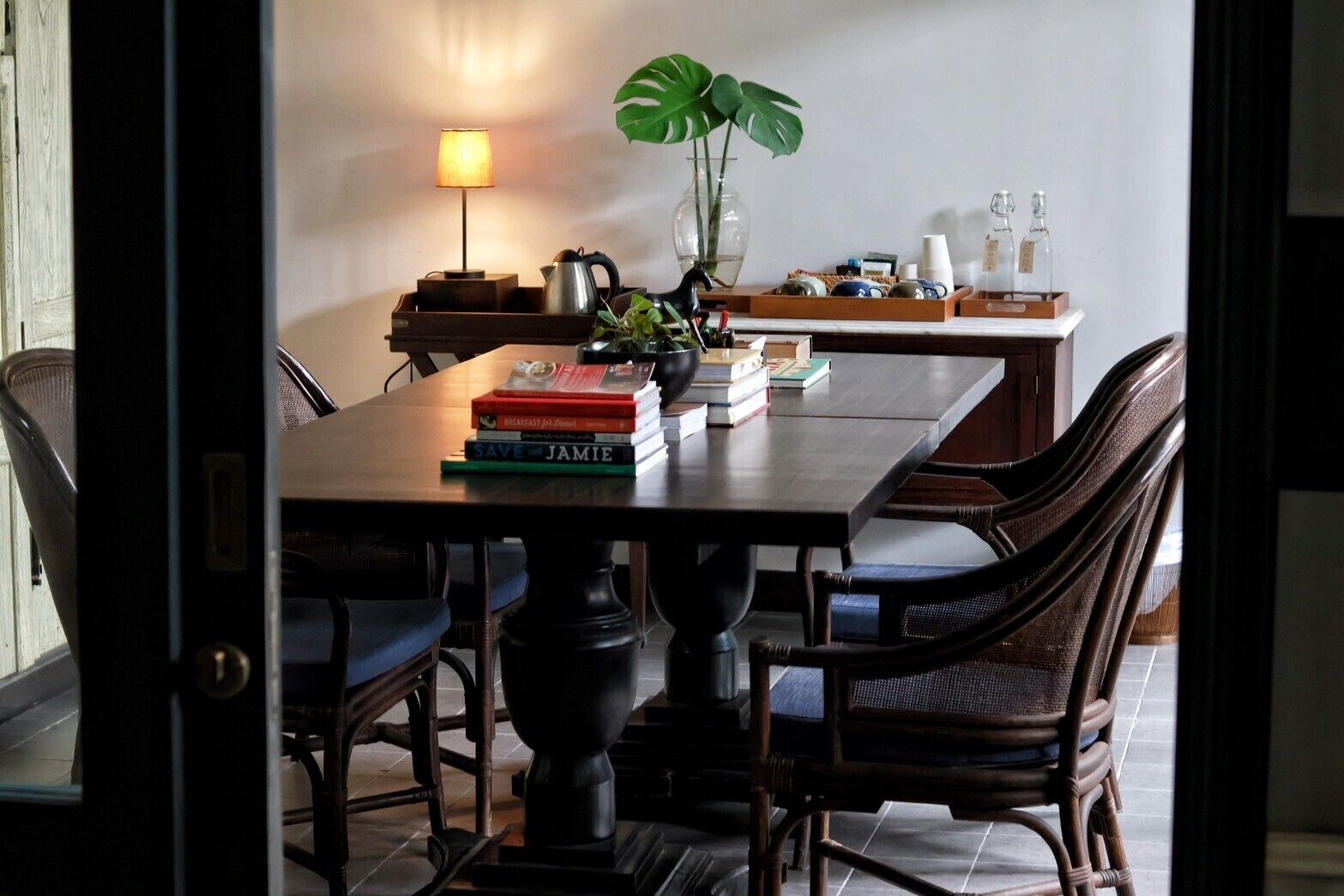 Et spiseområde med et bord, stole, en lampe, en plante og forskellige genstande på bordet.
