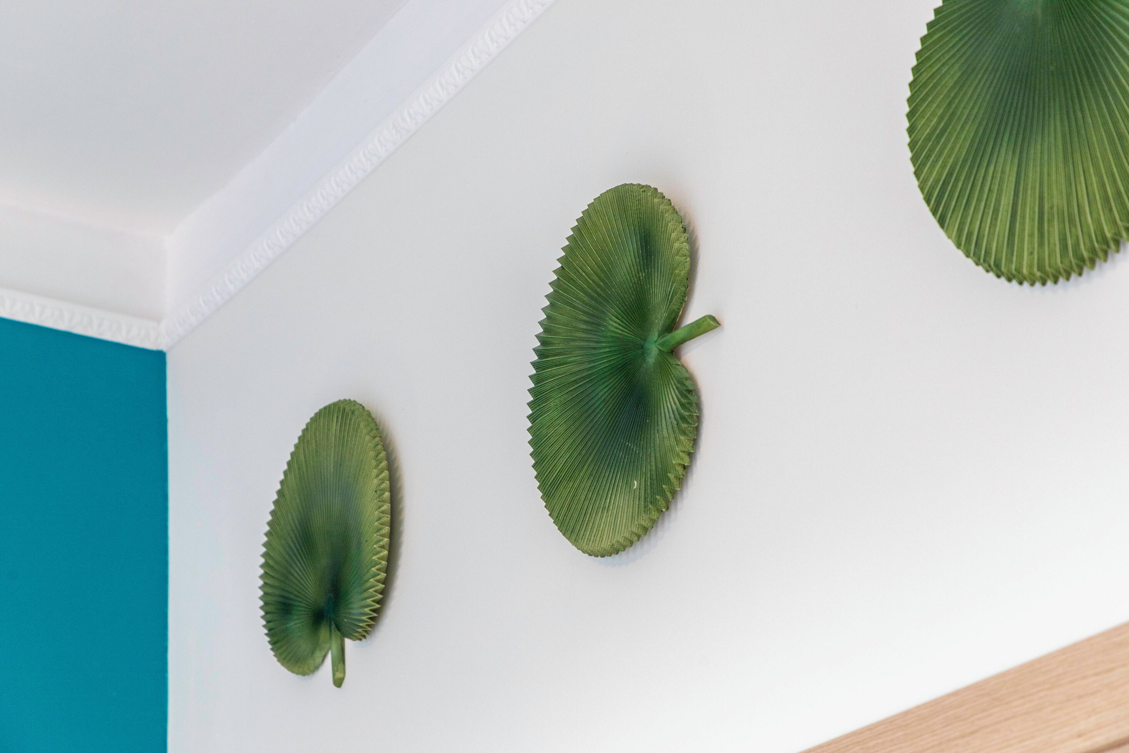 A white wall with three green, leaf-shaped objects.