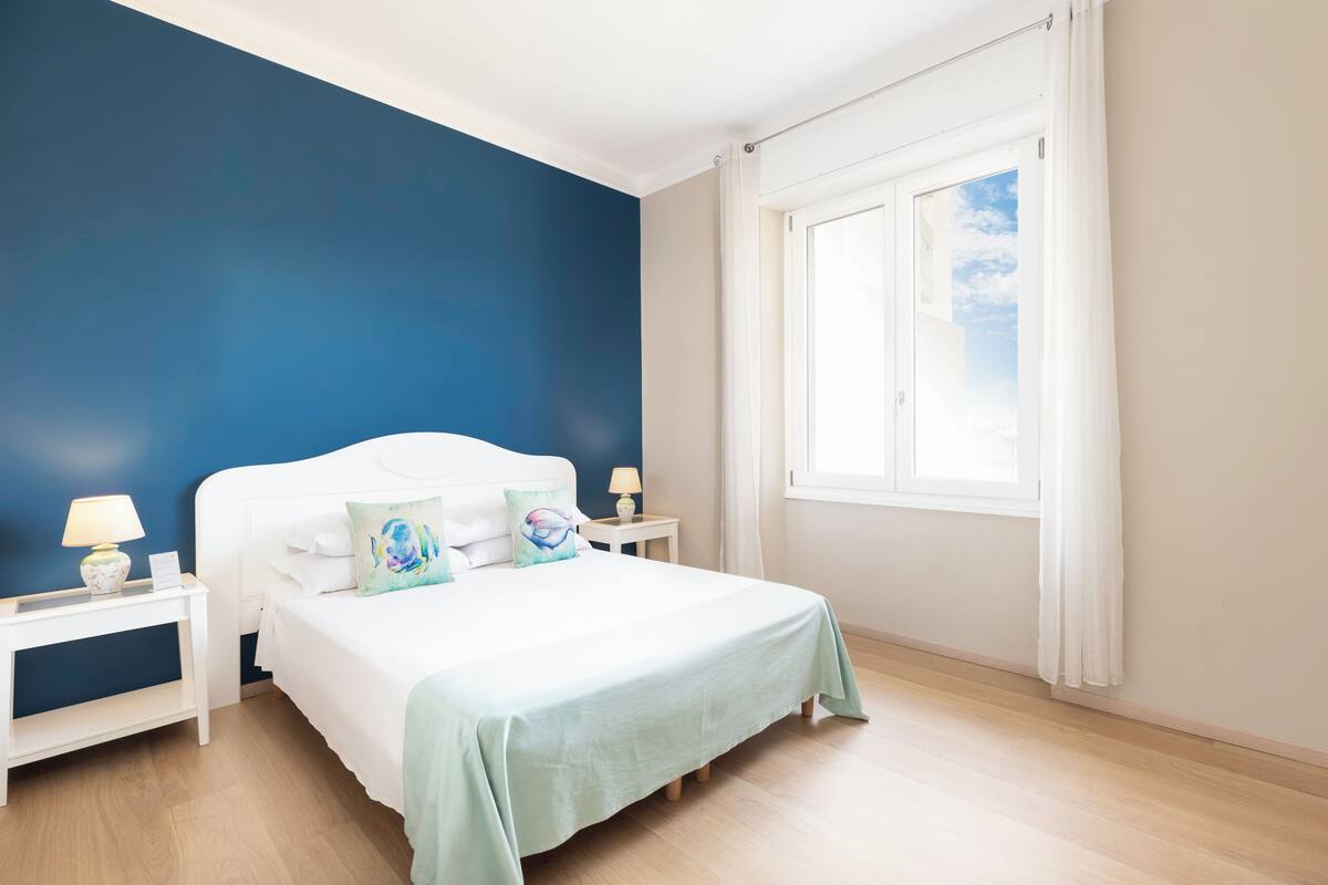 A bedroom with a bed, nightstands, a window, and a view of the sky.