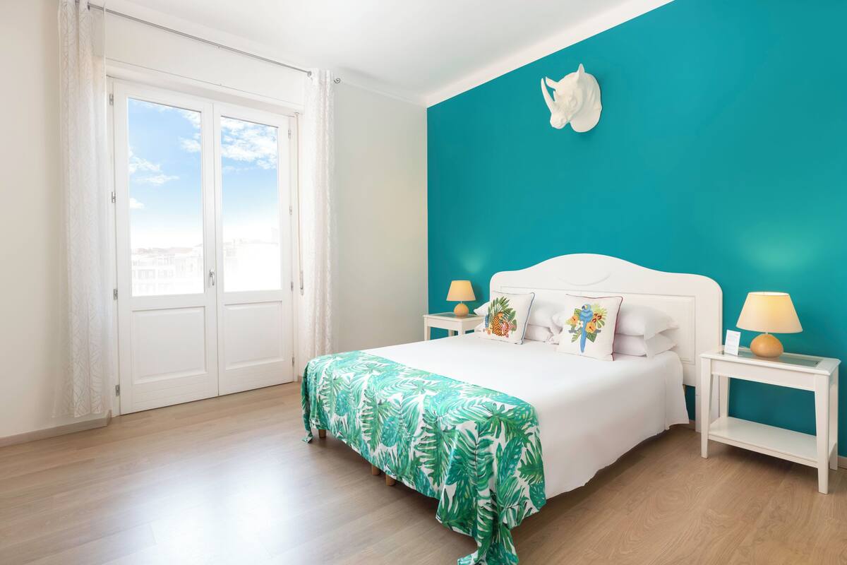 A bedroom with a bed, two bedside tables, a wall-mounted sculpture, and a view through a door.