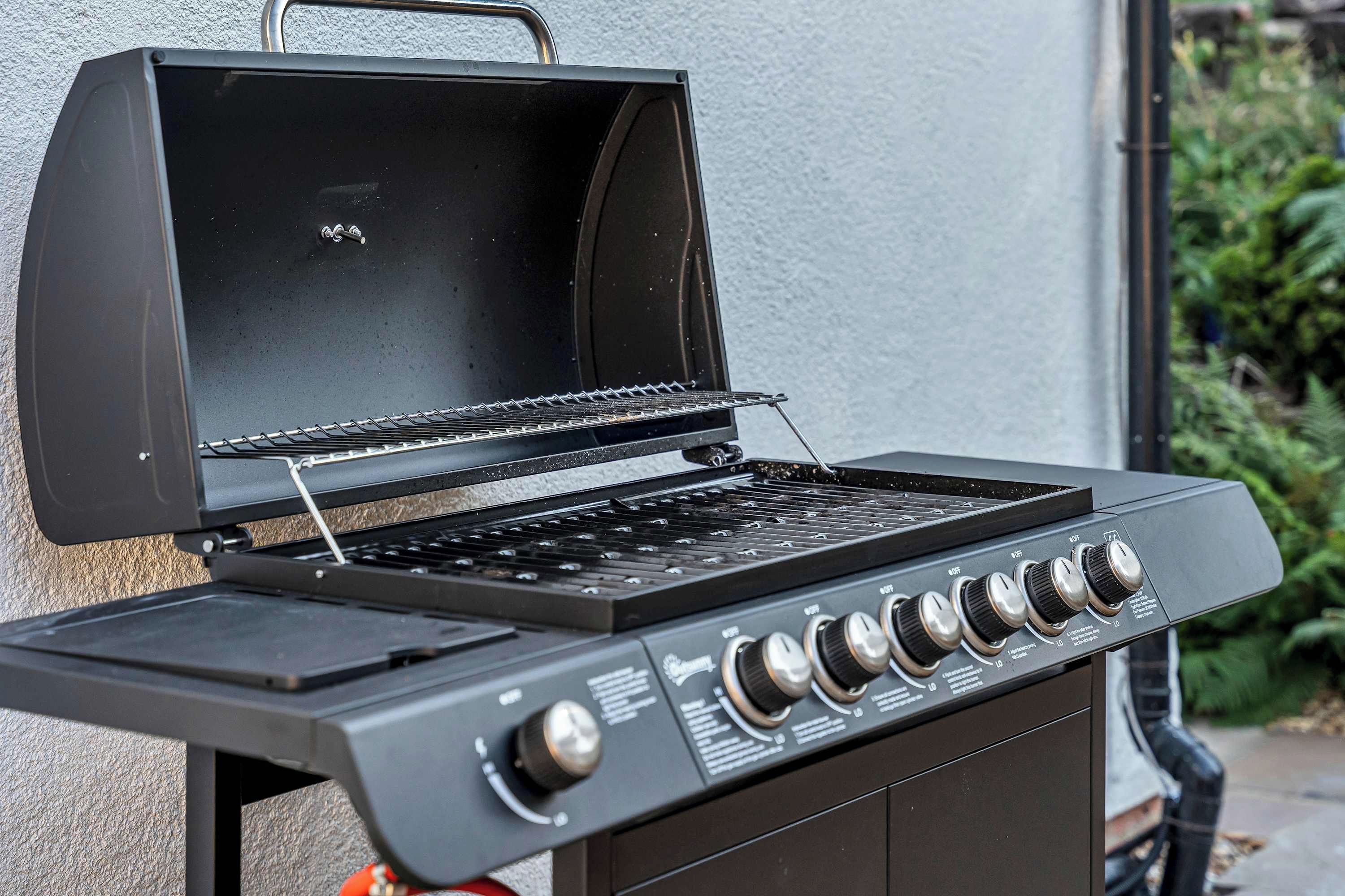 Una parrilla negra con quemador lateral y un panel de control con perillas.