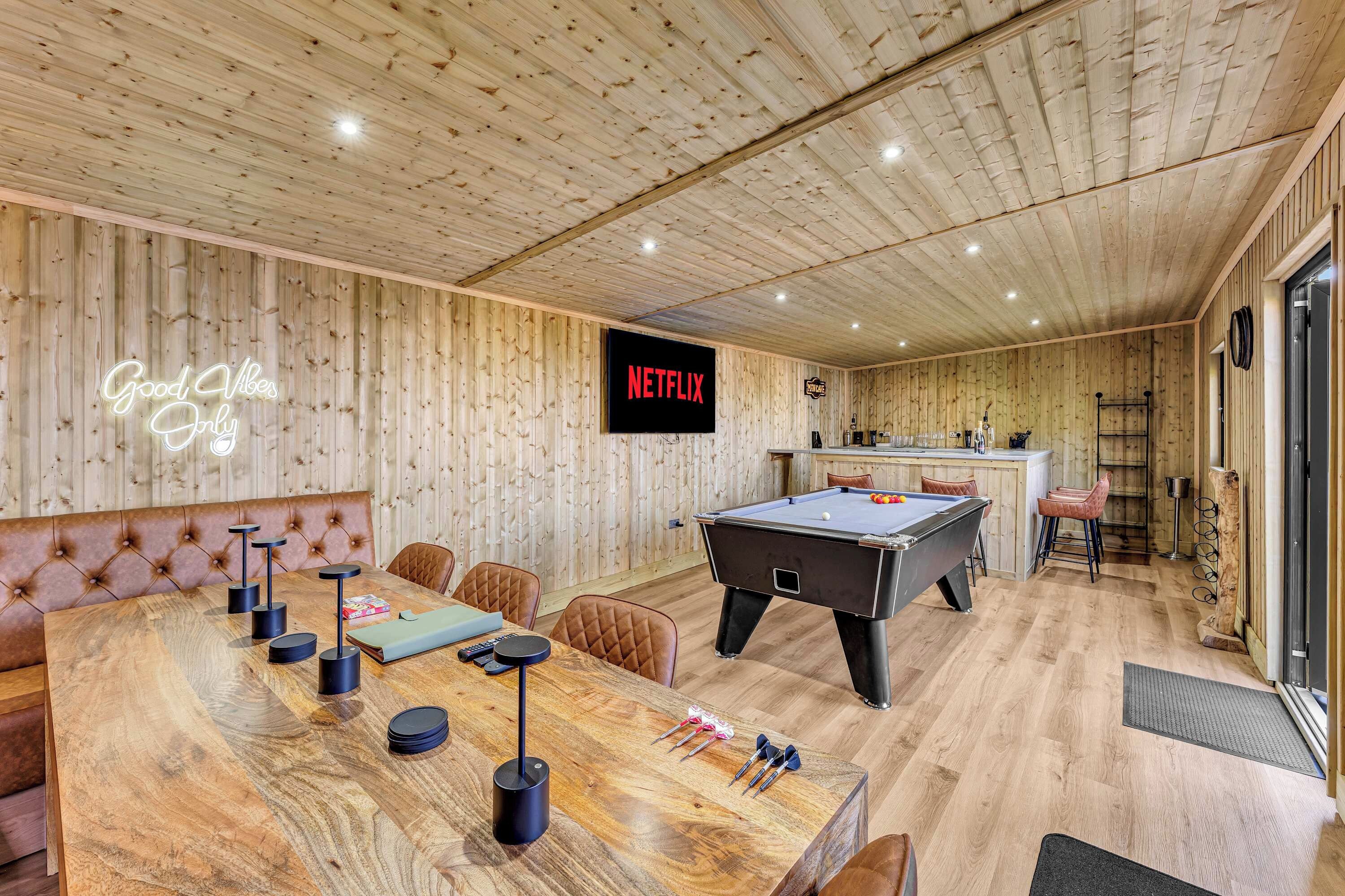 Ein Zimmer mit Holzwänden, einem Billardtisch, einem Neonzeichen, einem Fernseher, der Netflix anzeigt, und einer Bar.