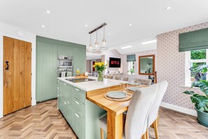 A modern kitchen with a central island, a dining area with a wooden table, and a living space with a television. - Stylish Country Retreat-HotTub•Fire Pit•Games Barn (Helsby)