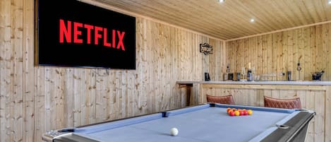 A pool table with a billiard cue, a pool ball, and a sign reading 'NETFLIX' on the wall.