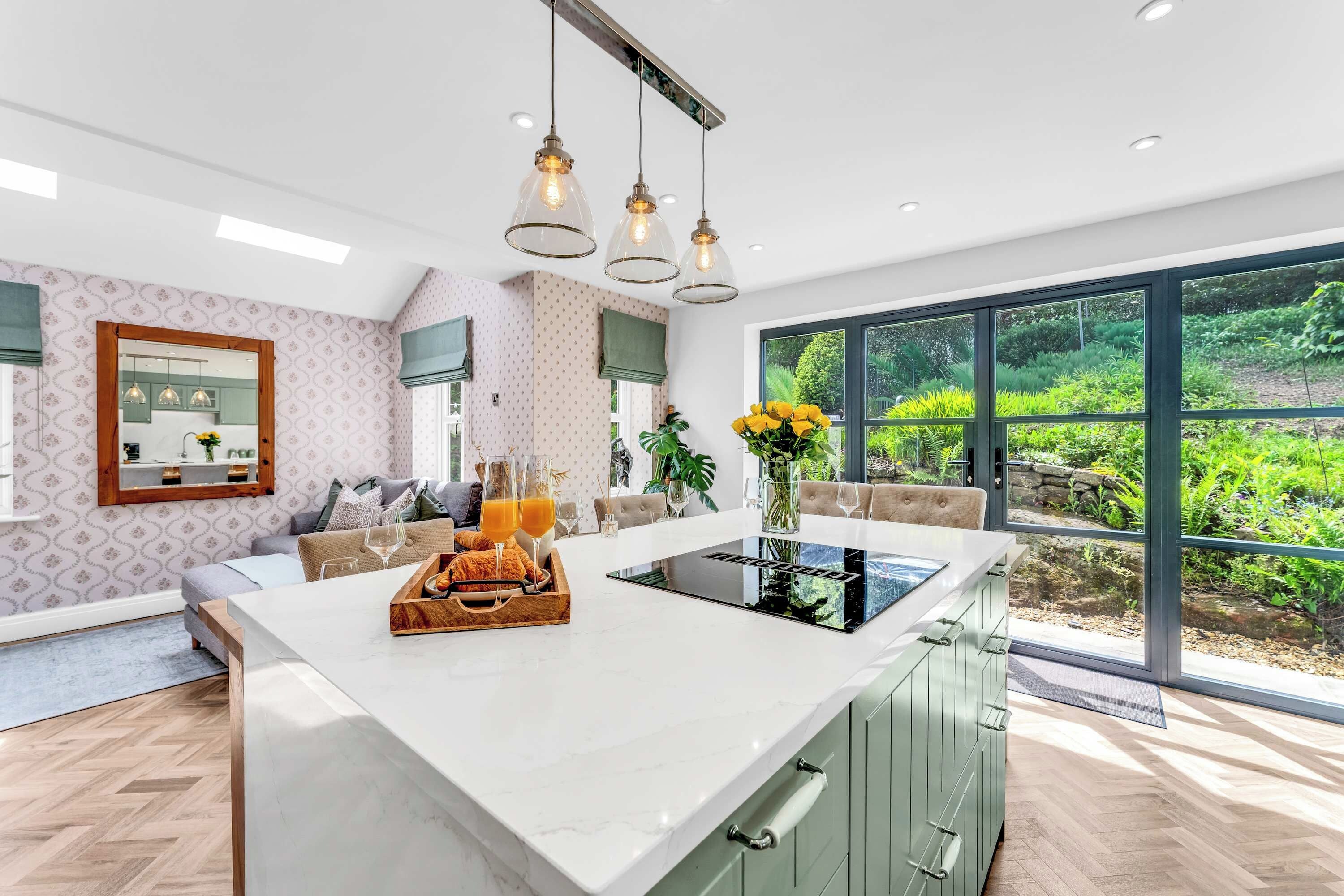 A modern kitchen with a central island, large windows, and a view of greenery.