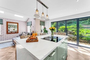 A modern kitchen with a central island, large windows, and a view of greenery. - Stylish Country Retreat-HotTub•Fire Pit•Games Barn (Helsby)