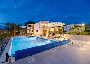 A swimming pool with lounge chairs, a covered seating area, and a modern house in the background. - Holiday Home Tanja Vir with heated pool (Vir)