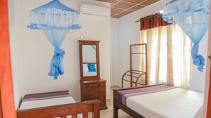 Un dormitorio con dos camas, una silla de madera, un espejo y un ventilador de techo.