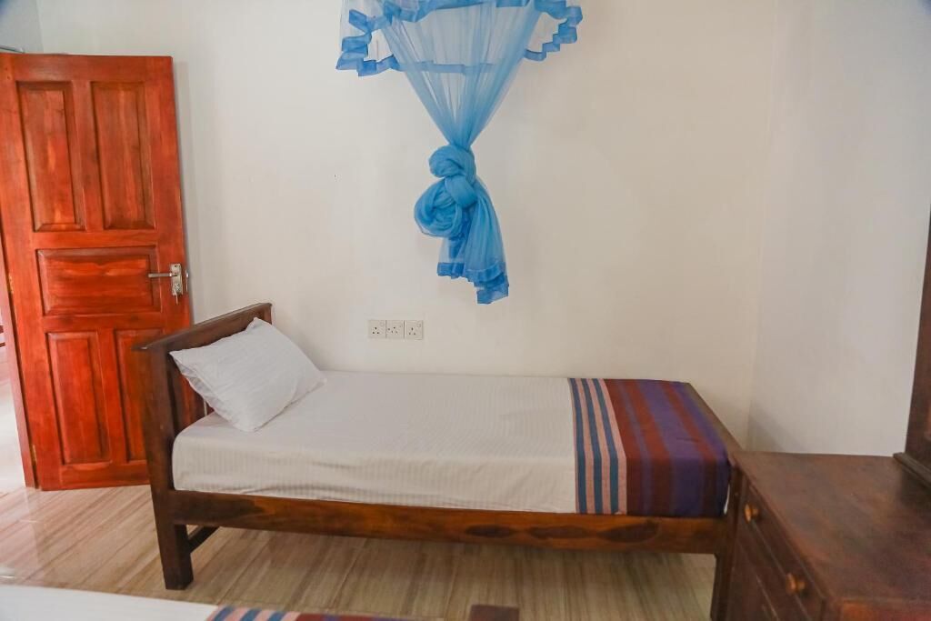 A single bed with a white pillow and a striped blanket, a wooden door, and a blue mosquito net hanging from the ceiling.