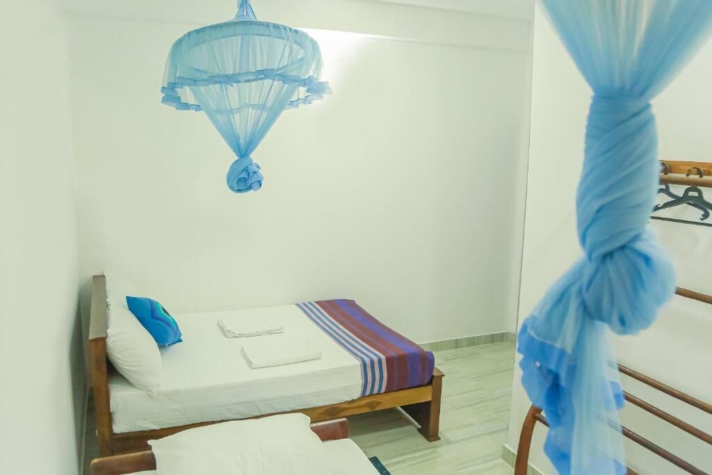 A small, single-bed room with a wooden frame, a white mattress, a blue pillow, a striped blanket, and a blue canopy.