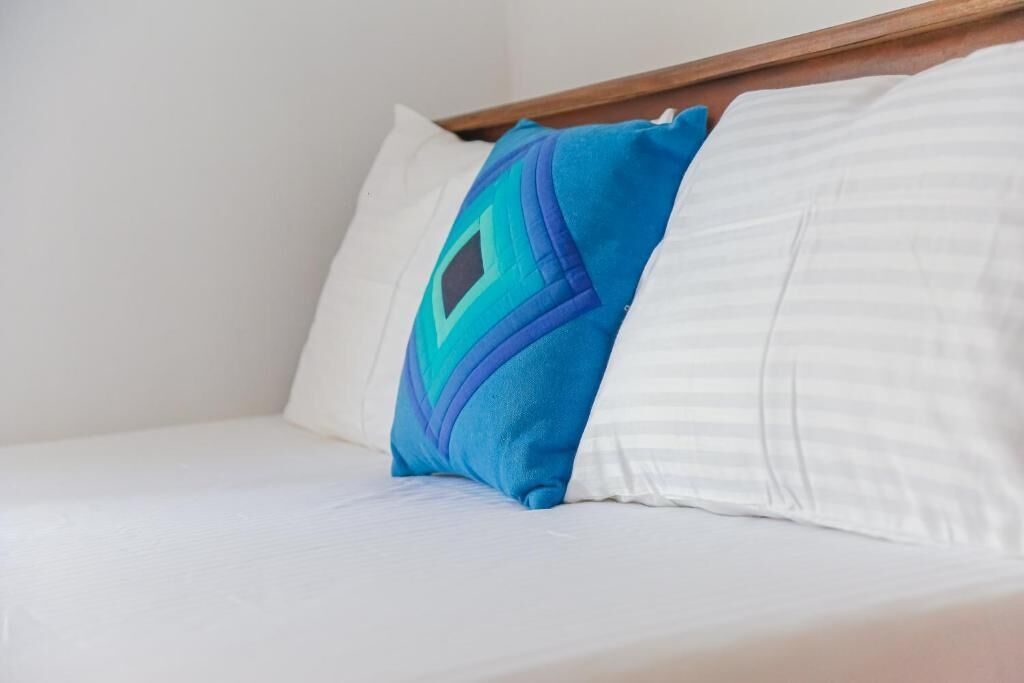 Una cama con ropa blanca y dos almohadas, una con estampado geométrico.