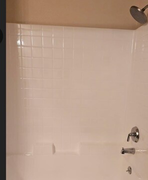 Ein Badezimmer mit weiß gefliesten Wänden, einer Duschbrause und einem Wasserhahn.