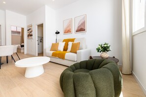 Ein modernes Wohnzimmer mit einem weißen Sofa, einem runden, grünen Sessel, einem weißen Couchtisch und einem Essbereich mit Tisch und Stühlen.