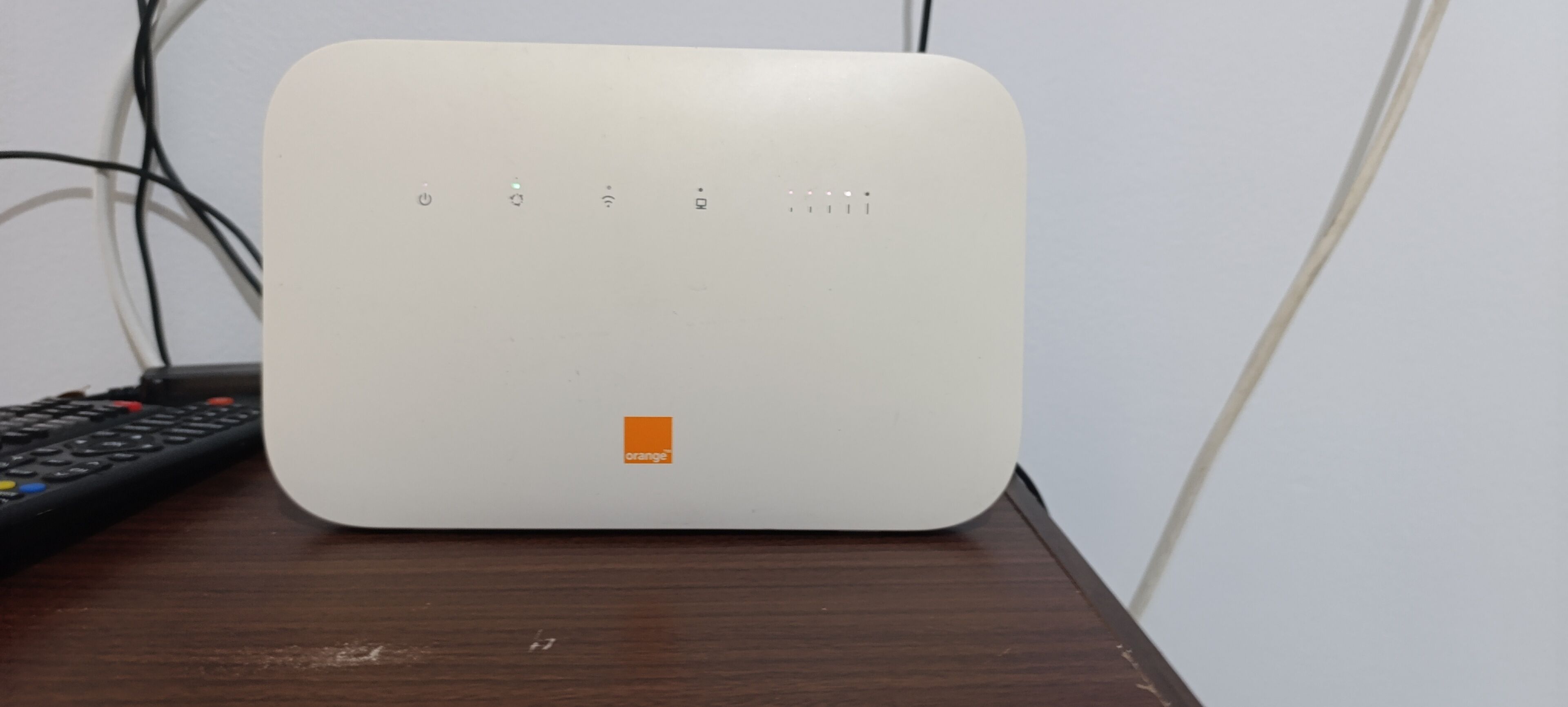 Un appareil électronique blanc doté d’un bouton d’alimentation, d’un symbole Wi-Fi et d’un petit logo orange, le tout posé sur une surface en bois.