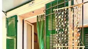 A building entrance with green shutters, a metal gate, and a curtain. - Hostdomus - Villino Matilde (Finale Ligure)