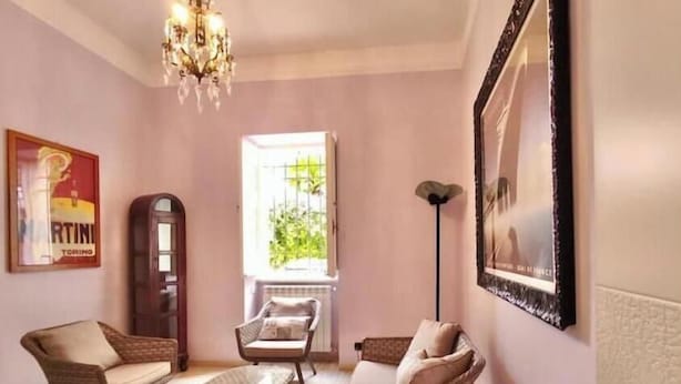 A living room with wicker furniture, a chandelier, a vintage telephone, and a poster on the wall. - Hostdomus - Villino Matilde (Finale Ligure)