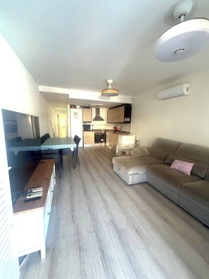 Ein modernes Wohnzimmer mit Sofa, Esstisch mit Stühlen, Küchenzeile mit Schränken und Deckenventilator.