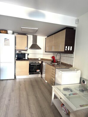 Eine moderne Küche mit Holzausstattung, einer Edelstahl-Dunstabzugshaube, einem eingebauten Backofen, einer Spülmaschine und einem Glastisch mit Wasserkocher.